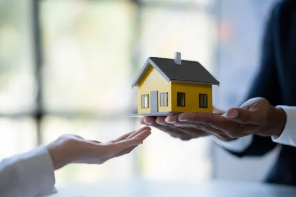 Manos entregan un modelo de casa para venta inmobiliaria.